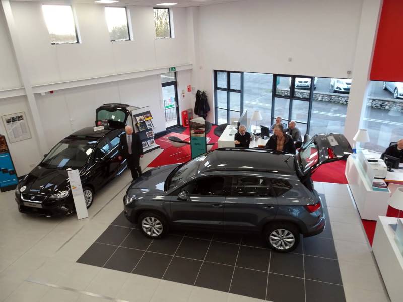 Car showroom with two vehicles on display and people at desks